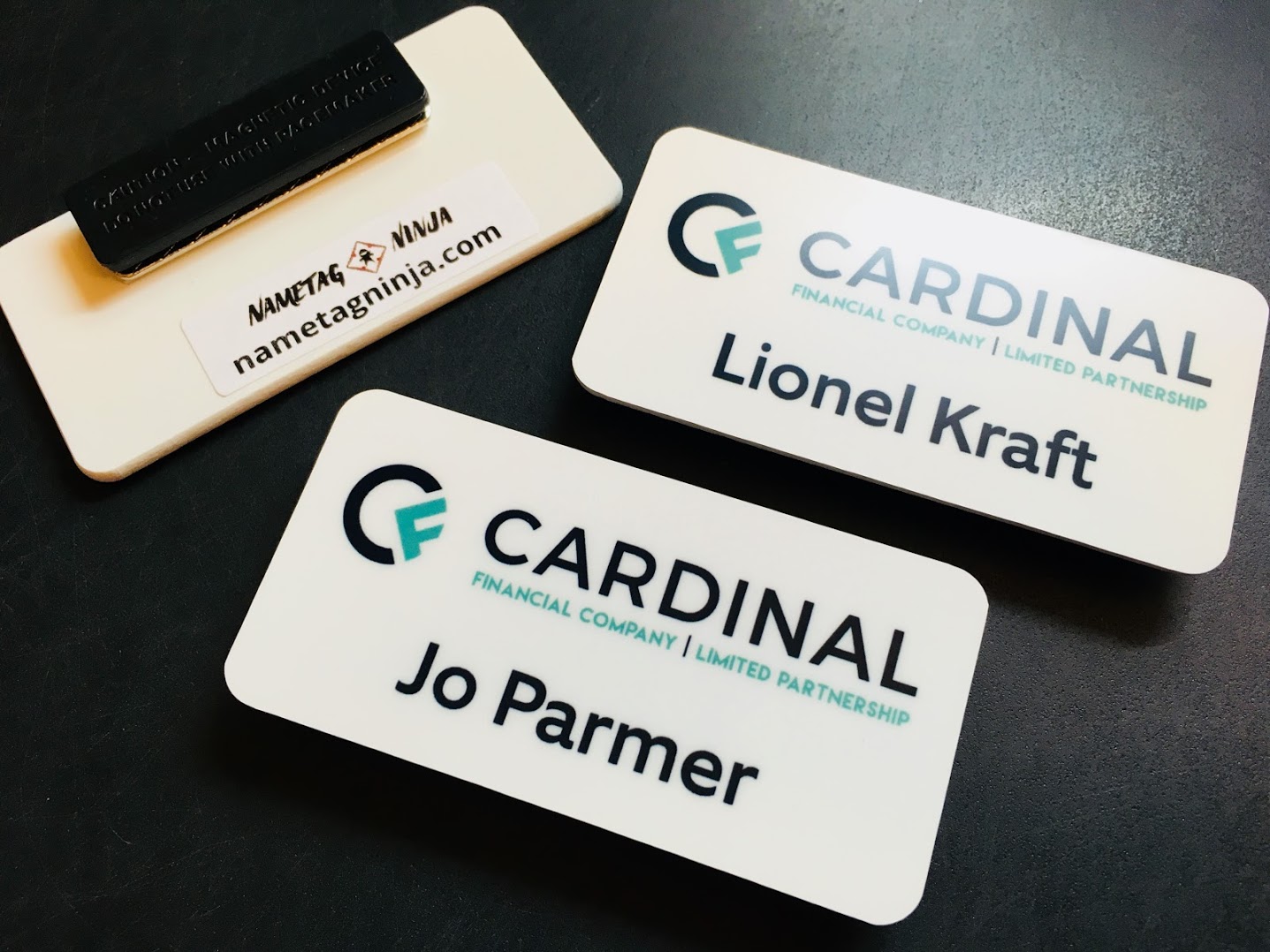 A collection of white plastic nametags, photo showing front and back of the product. Logo is for Cardinal Financial Company.
