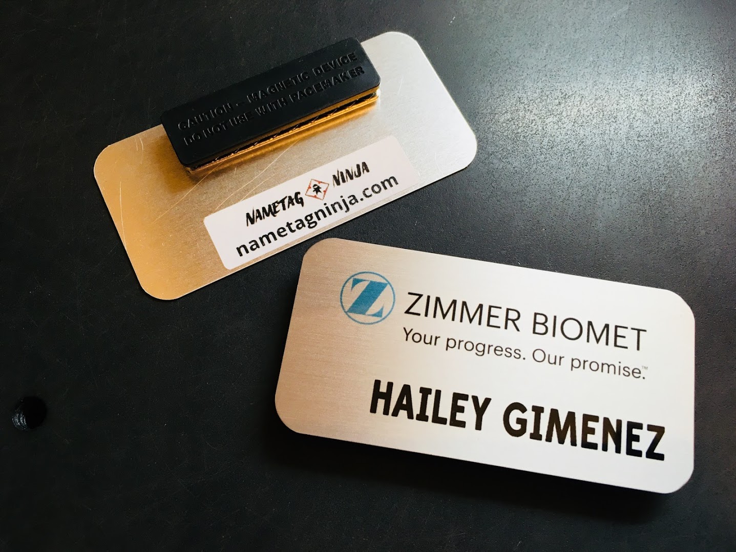 Brushed silver name badge. Photo shows front and back of the product. Design is for Zimmer Biomet.