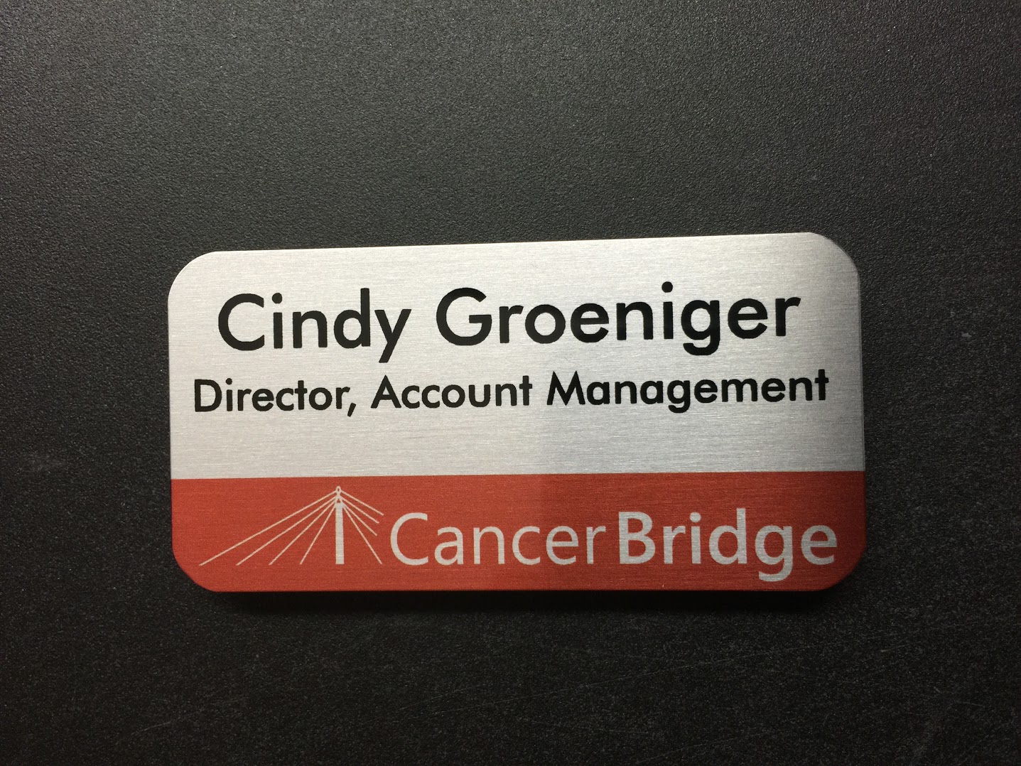 A brushed silver nametag. Design is for Cancer Bridge.